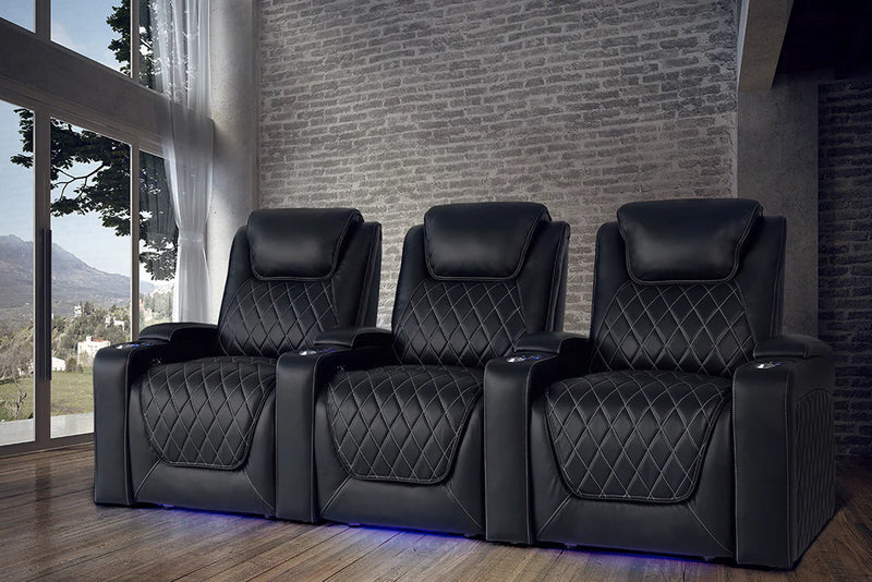 The Valencia Oslo XL Home Theater Seating in the row of 3 configuration and black color in a room with a brick wall and a window with a view of a mountain
